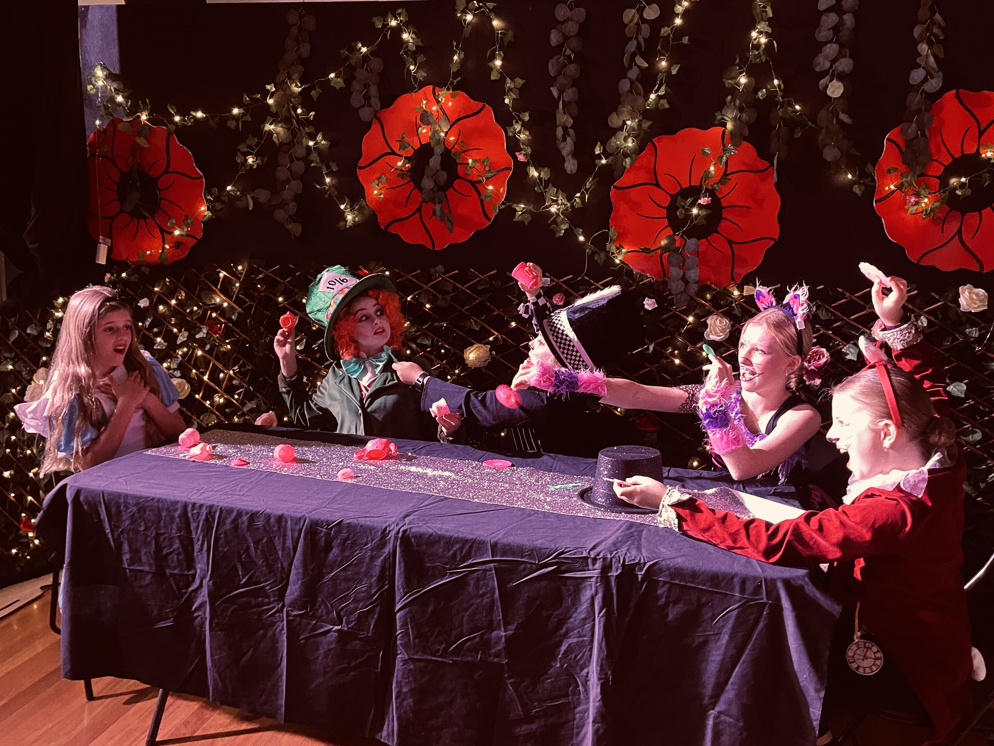 A scene from our 2022 school musical Alice in wonderland, 4 colourful characters sit around the mad hatters tea party